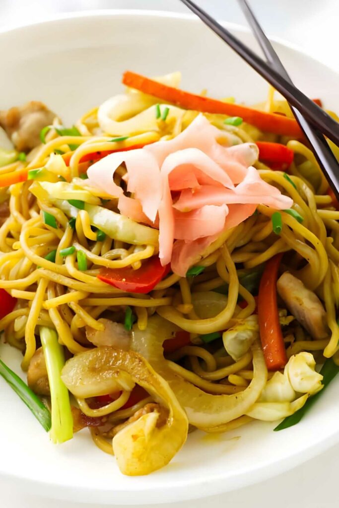 Pork yakisoba served with pickled ginger and chopsticks.