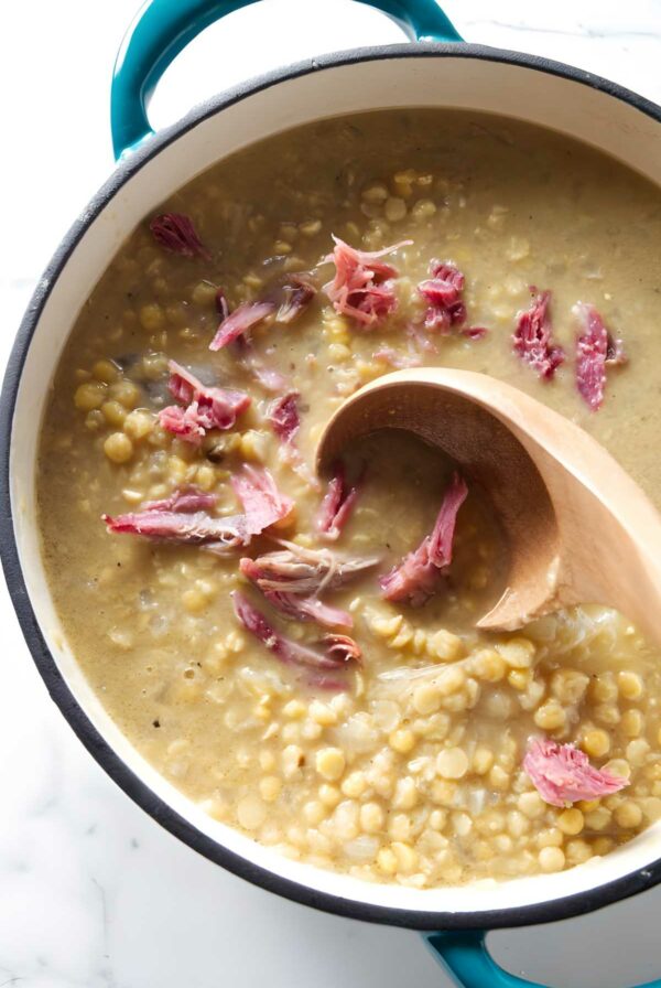 Pot of Swedish pea soup with ham, stirred by a wooden spoon.