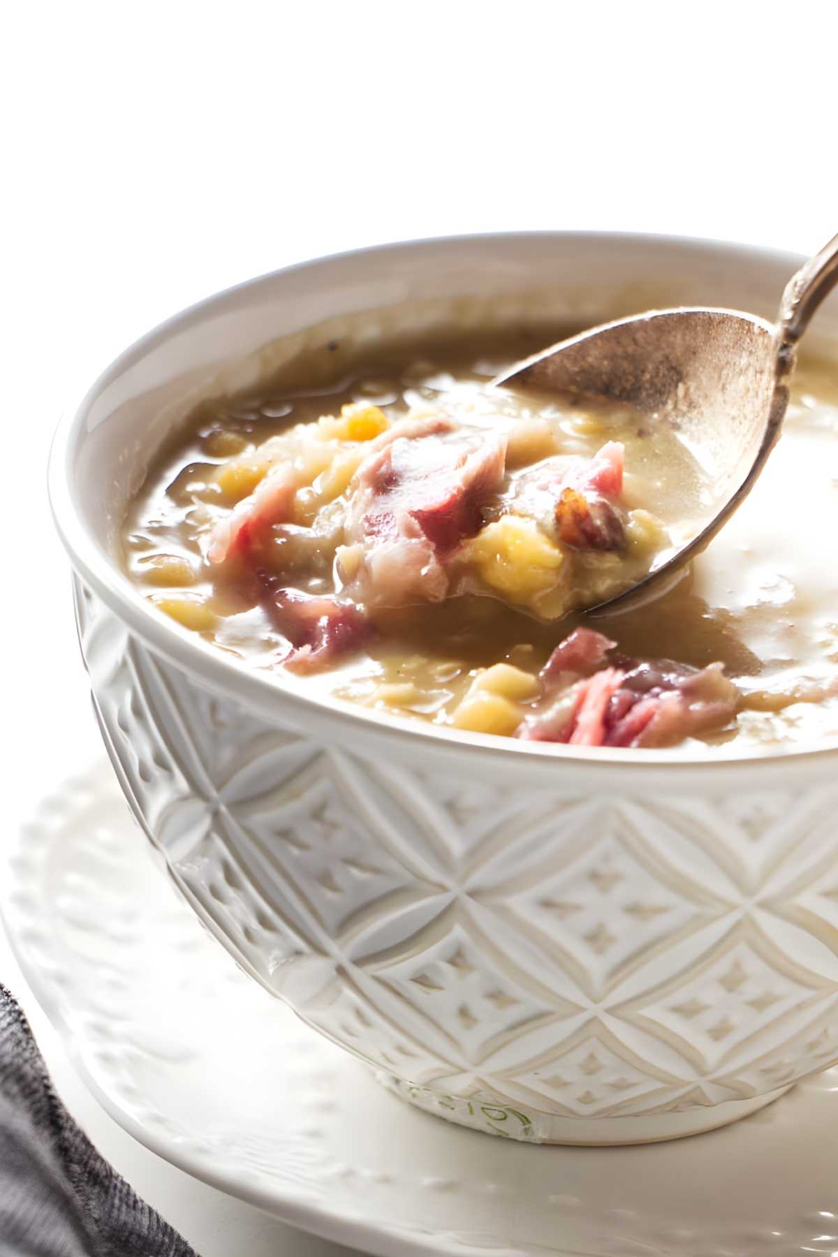 Close-up of soup with ham and vegetables, spoon lifting portion from bowl.