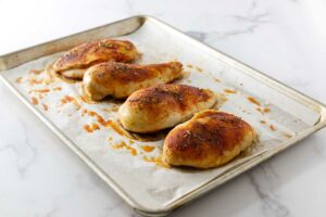 Four baked chicken breasts on a sheet pan.