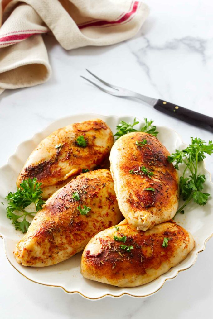 Seasoned chicken breasts on a platter with parsley.