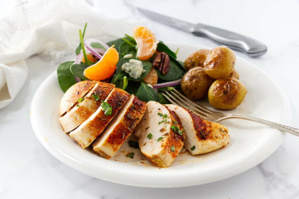 A dinner plate with a sliced chicken breast next to a salad and roasted potatoes.