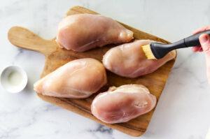 Brushing oil over four chicken breasts.