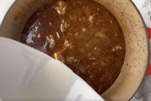 Adding a cornstarch slurry to beef tips in a pot.