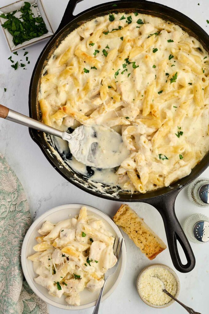 A spoon scooping alfredo pasta bake from a casserole.
