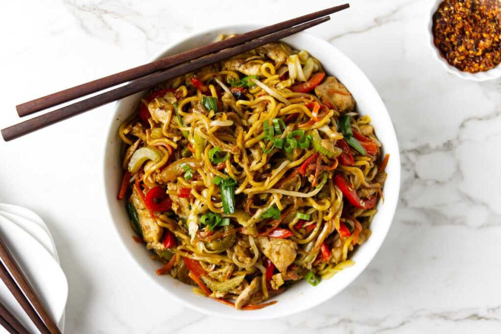 Chicken chow mein in a bowl next to chop sticks.