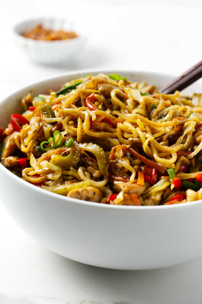 A serving bowl filled with stir fry chow mein with chicken.