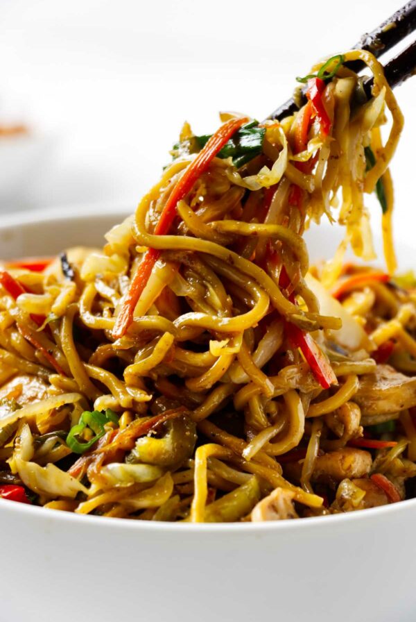 Chop sticks lifting chow mein noodles from a bowl.