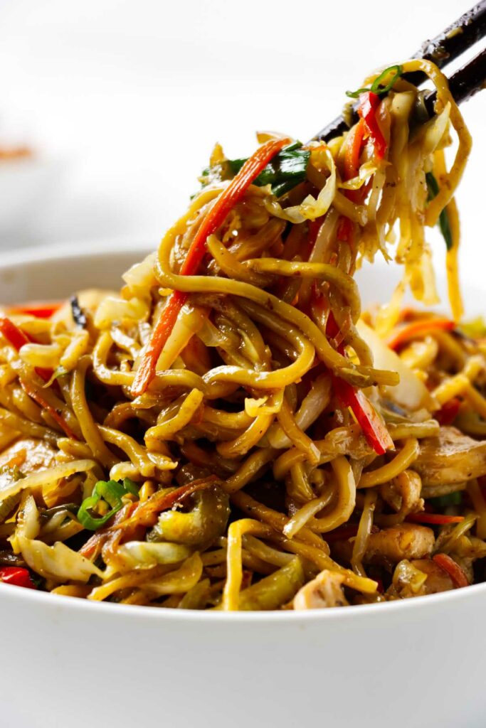 Chop sticks lifting chow mein noodles from a bowl.