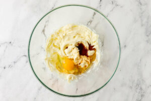 Adding an egg and vanilla extract to a mixing bowl.