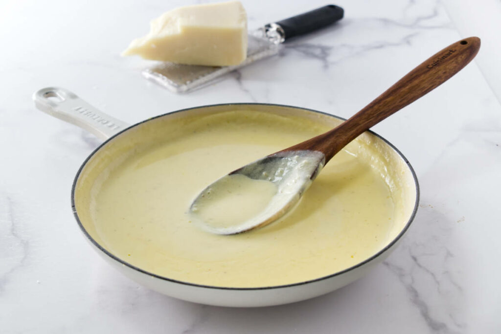A wooden spoon in a skillet with homemade alfredo sauce.