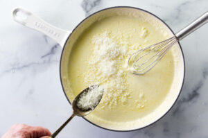 Adding parmesan cheese to white sauce.