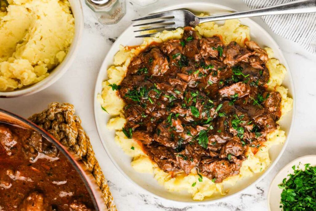 Mashed potatoes with beef tips and gravy topped with parsley garnish on a plate.