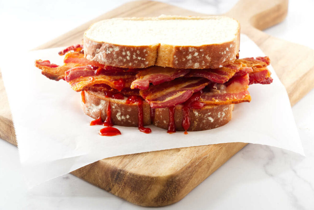 A stack of crispy bacon in a sandwich with white bread.
