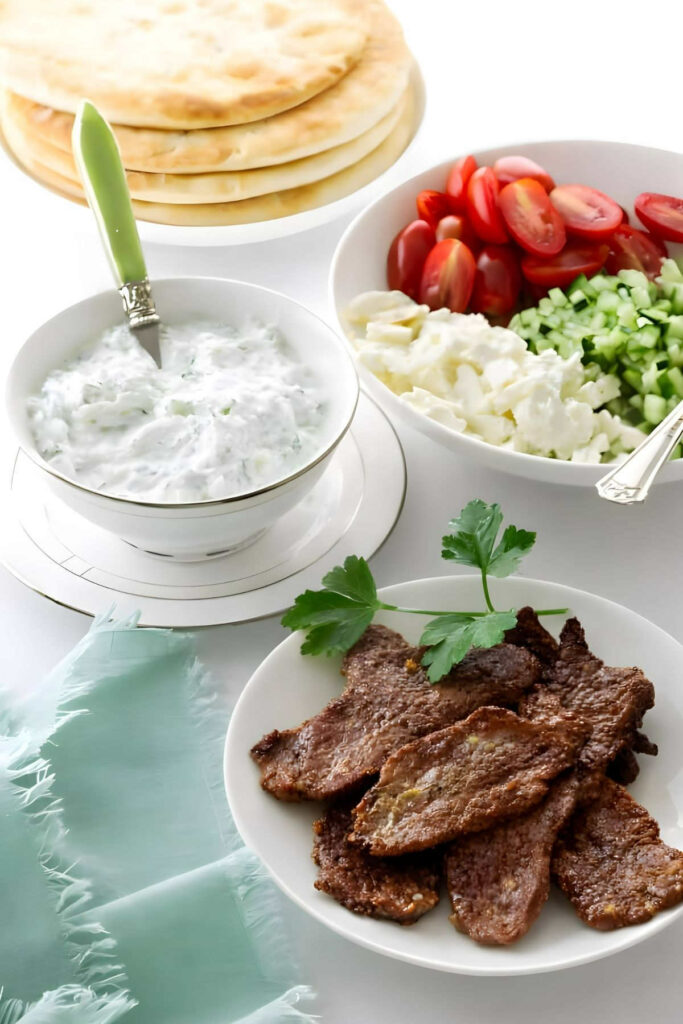Components for a lamb pita sandwich with slices of lamb and Tzatziki sauce.
