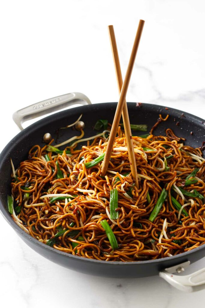 Chopsticks in the center of a skillet of pan fried noodles.