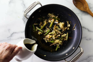 Adding the sauce to the skillet with the charred scallions.