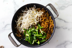 Tossing scallions and beans sprouts with the soy noodles.