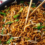 Stir fried noodles in a skillet with soy sauce and scallions.