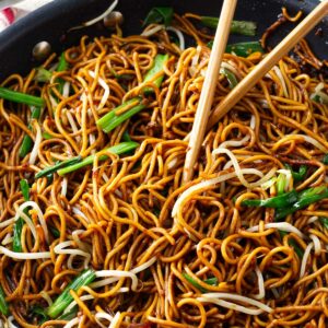 Stir fried noodles in a skillet with soy sauce and scallions.
