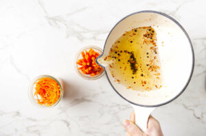 Pouring pickling brine into jars with carrot slices.