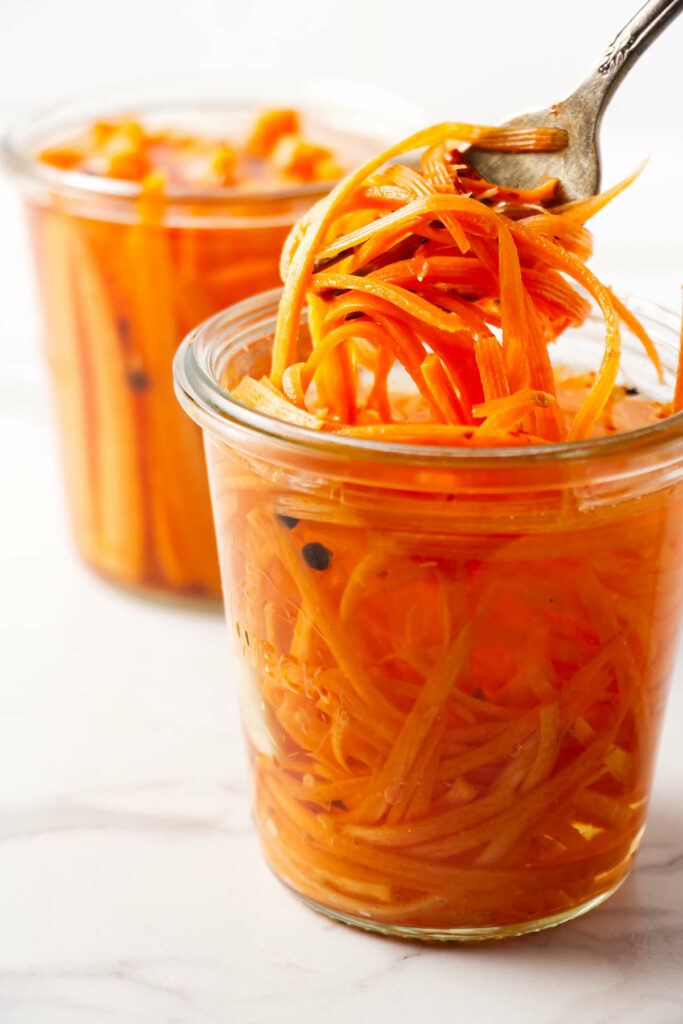 Lifting pickled carrot strips out of a jar.