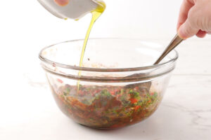 Drizzling oil into a red chimichurri mixture while stirring.