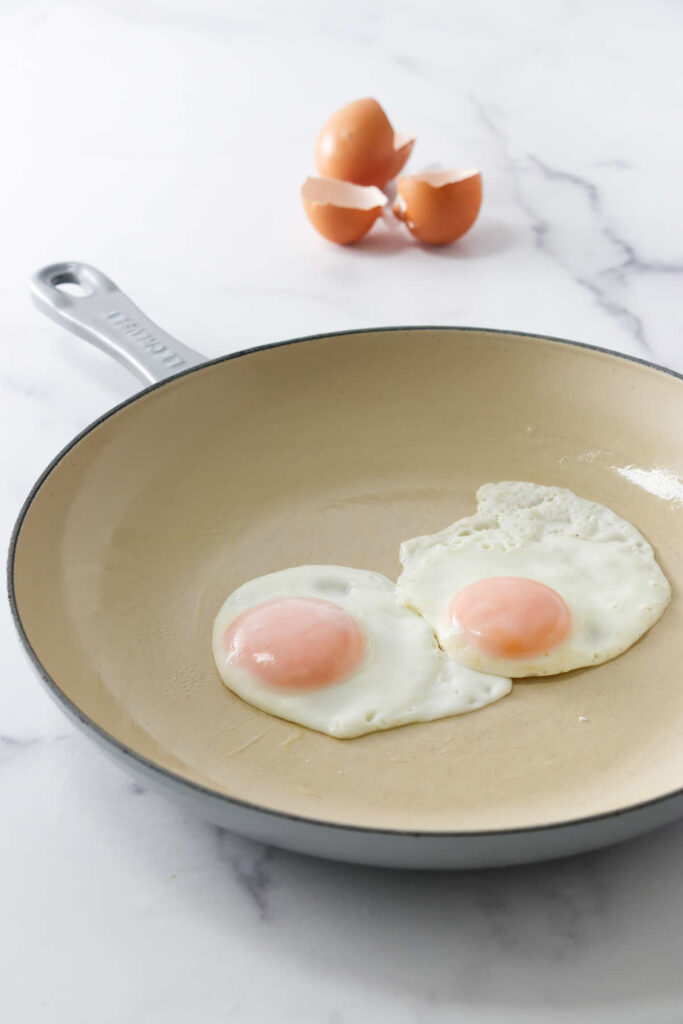 Two perfectly fried eggs in a skillet next to brown egg shells.