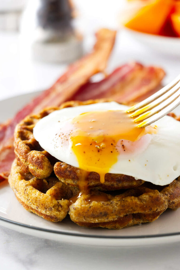 A fork breaking the yolk of a steam fried egg.