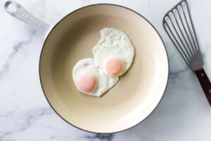Two perfectly fried eggs in a skillet next to a spatula.