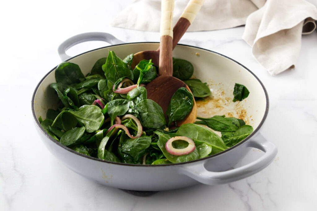 Bowl filled with fresh spinach and sliced onions.