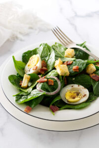 Plating a warm spinach salad on a dinner platter.