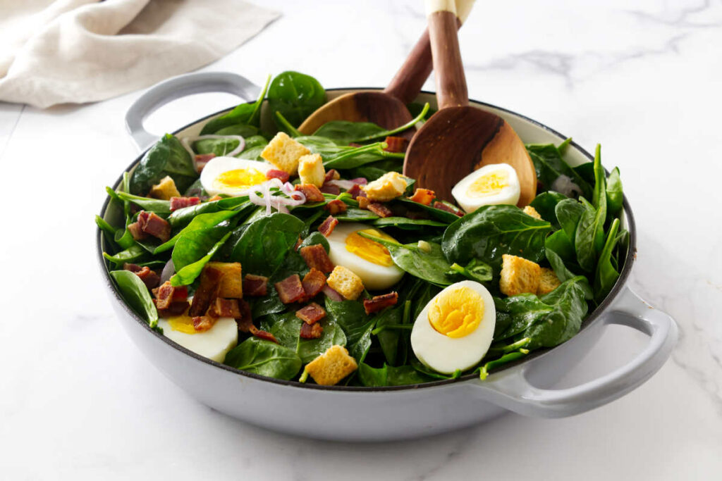 Tossing hot bacon dressing over a spinach salad.