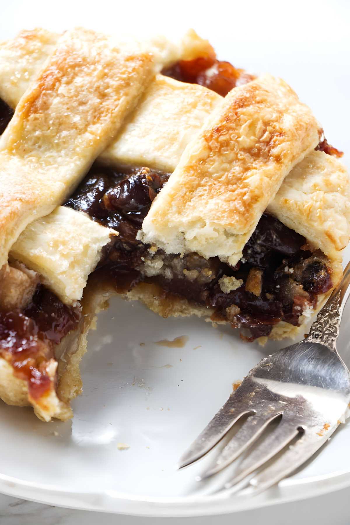 Slice of dried cherry tart with bite, on white plate beside fork.