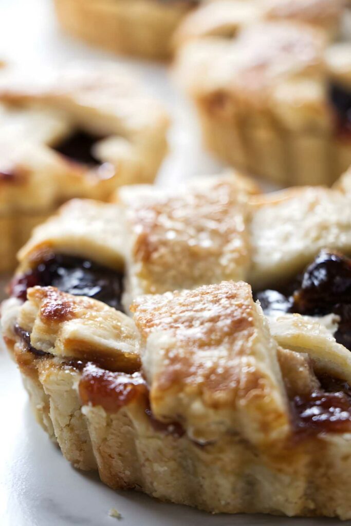 Mini dried cherry tarts with golden lattice crust and berry filling, close-up view.