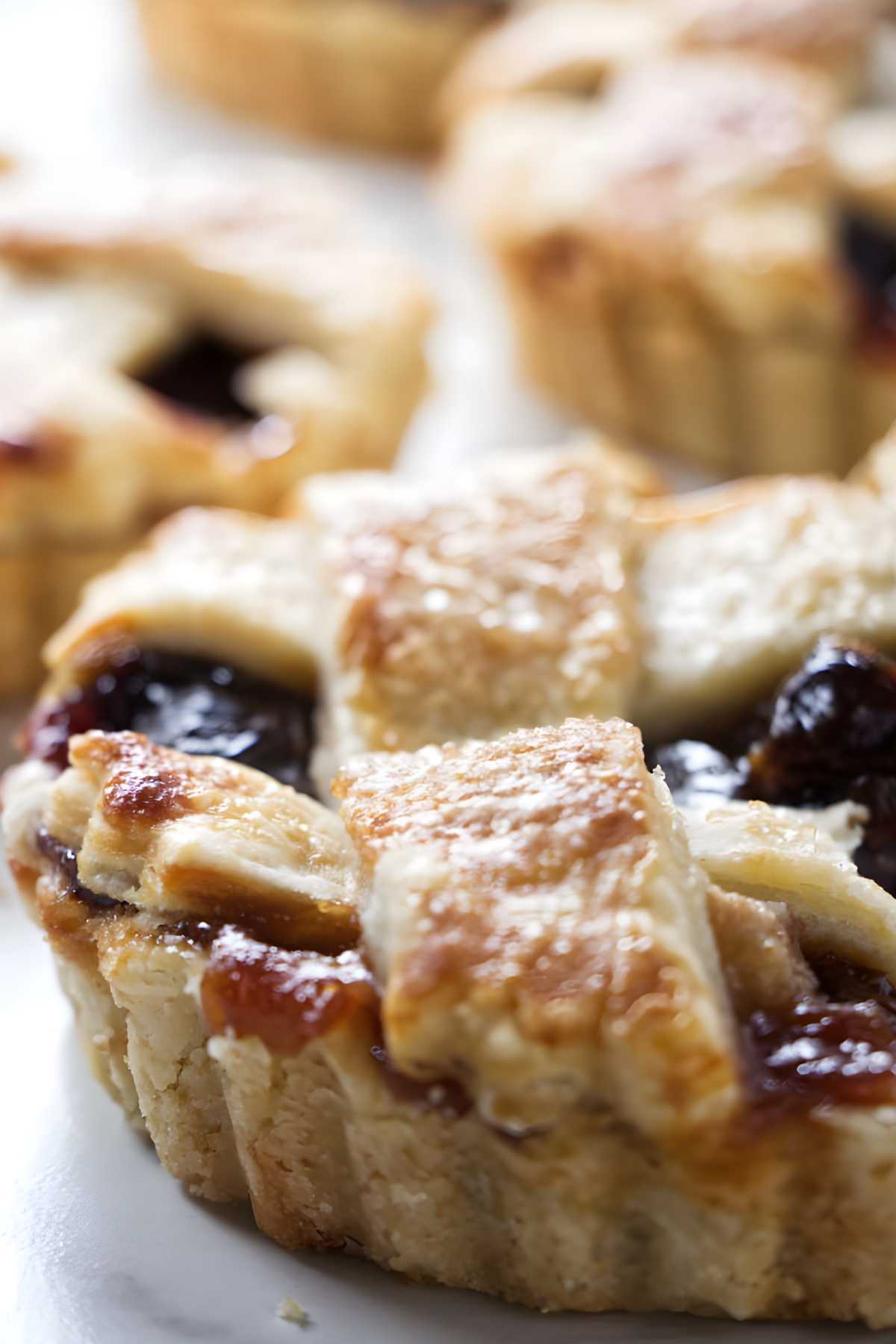 Mini dried cherry tarts with golden lattice crust and berry filling, close-up view.