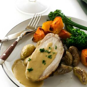 Plate of roasted pork with gravy, potatoes, broccoli, and pumpkin.
