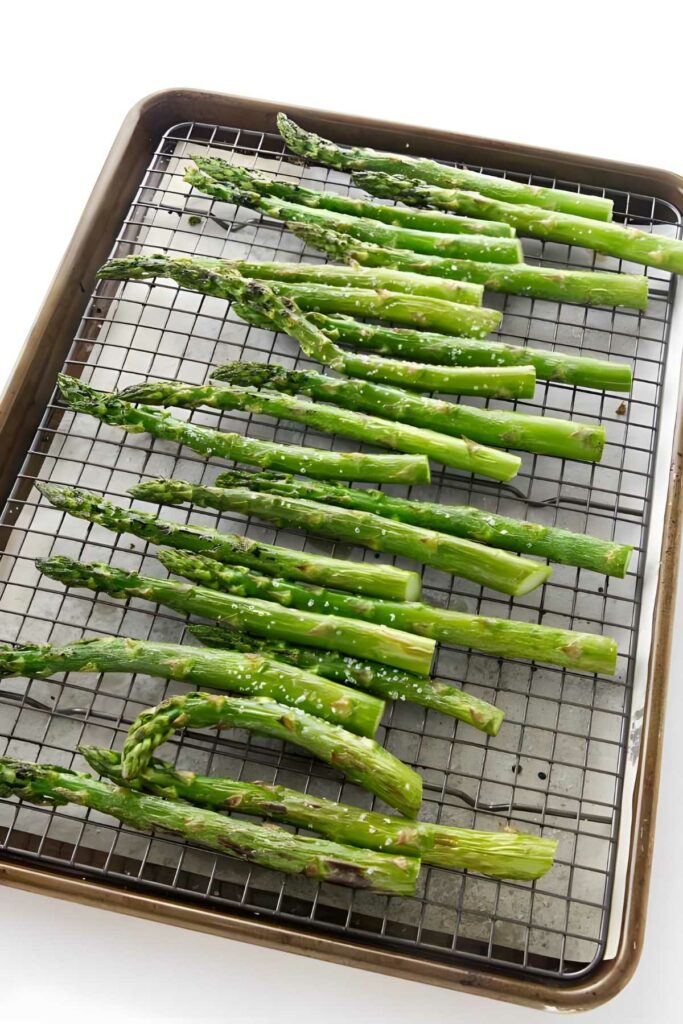 Uncooked asparagus spears seasoned on a wire rack before roasting.