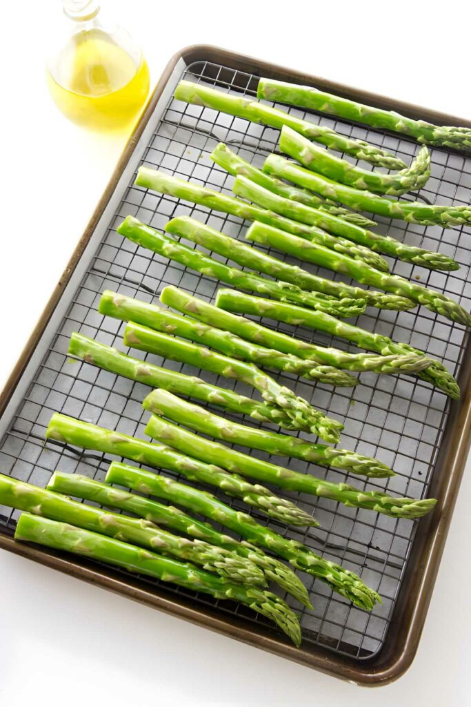 Asparagus spears arranged on a wire rack with an olive oil bottle nearby.
