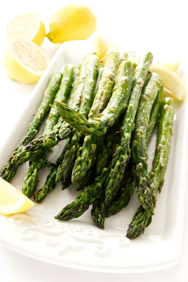 Roasted asparagus with lemon wedges on a plate, lemons in background.
