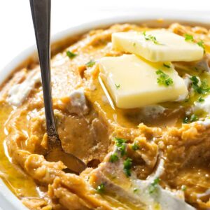 Bowl of mashed sweet potatoes with butter, herbs, and a spoon.