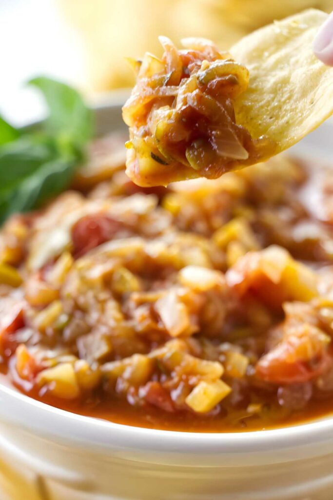 Tortilla chip scooping chunky salsa from a white bowl, close-up view.