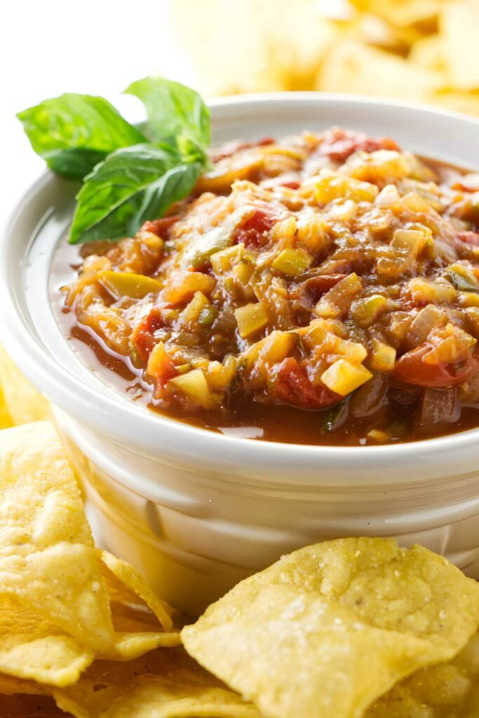 Bowl of chunky zucchini salsa with basil and yellow tortilla chips.