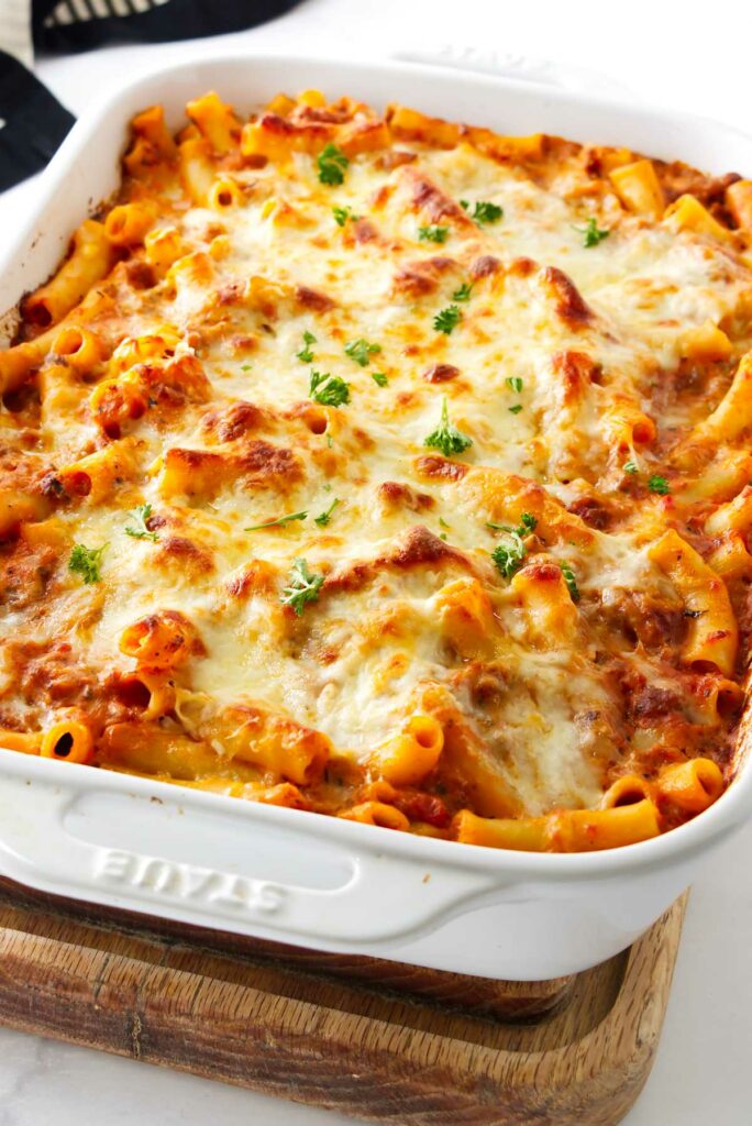 A white baking dish filled with baked ziti pasta with cheese.