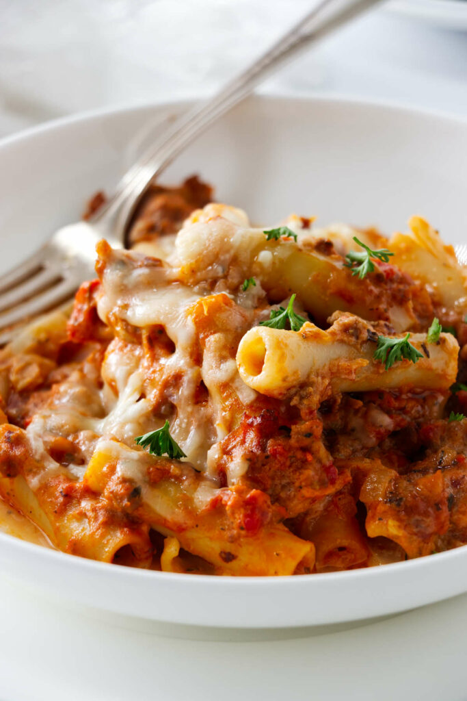 A serving bowl filled with baked ziti with italian sausage.