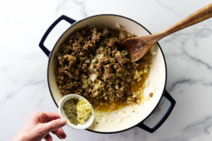 Adding spices to the sausage in a skillet.