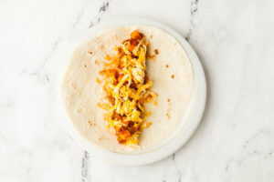 Adding sausage, potatoes and cheese to a flour tortilla.