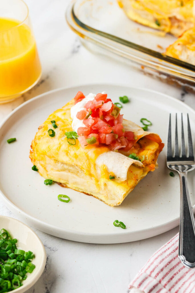 A serving of enchilada breakfast casserole on a plate next to a fork.