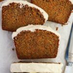 Three slices of carrot cake with frosting on parchment, knife beside them.