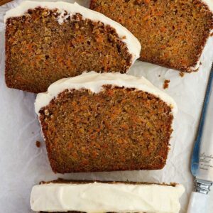 Three slices of carrot cake with frosting on parchment, knife beside them.